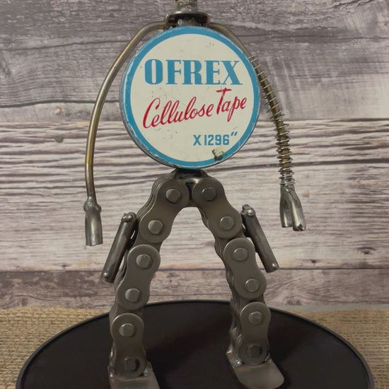 Meet Rex!  This one-of-a-kind robot scrap art sculpture is made from a vintage round cellulose tape tin body, a commemorative USA tin salt shaker head, lamp parts and spring arms, industrial chain legs each strapped with a pistol ready for action. Spruce up any shelf in your home or office with this super cool robot sculpture.  