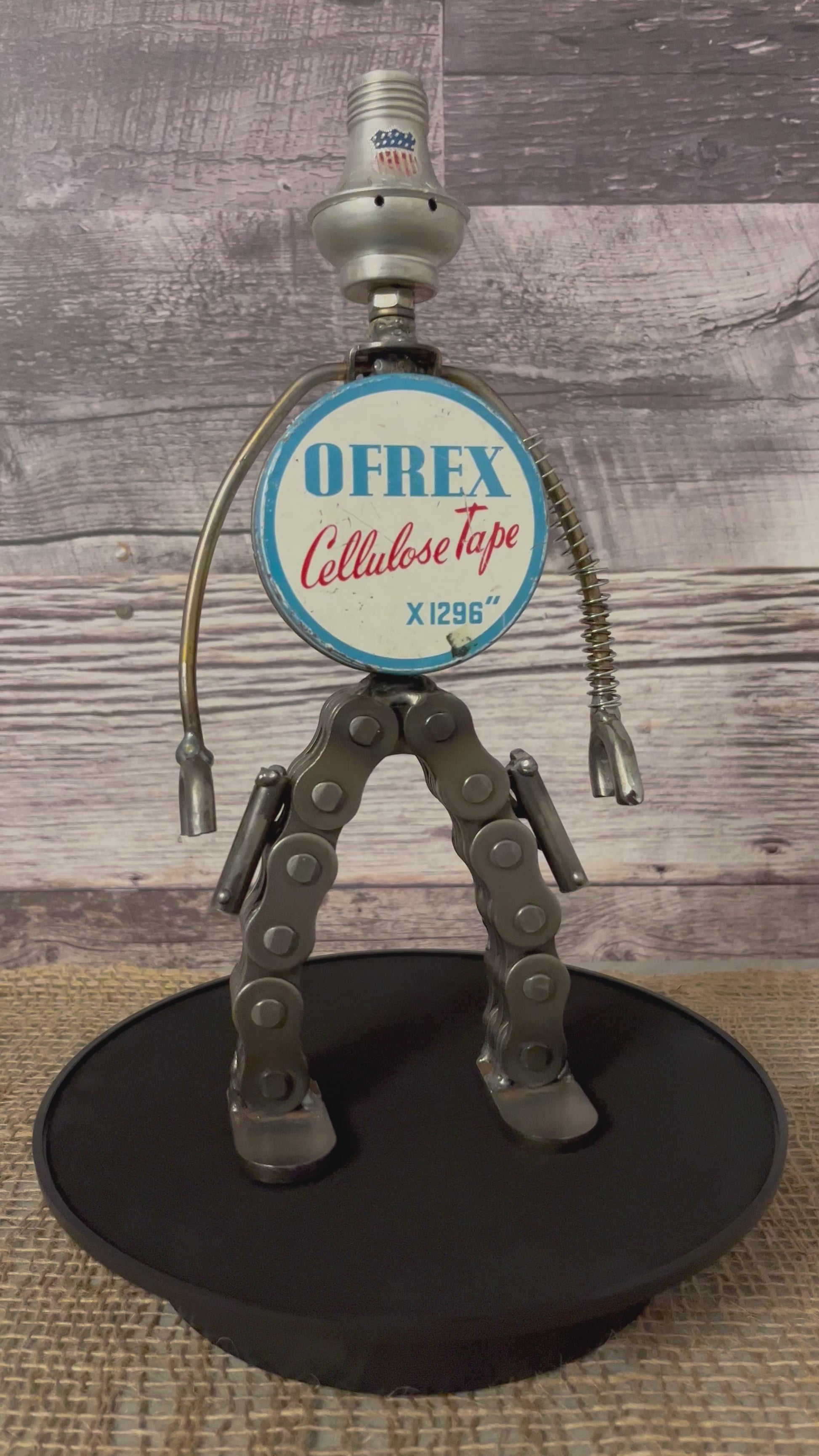Meet Rex!  This one-of-a-kind robot scrap art sculpture is made from a vintage round cellulose tape tin body, a commemorative USA tin salt shaker head, lamp parts and spring arms, industrial chain legs each strapped with a pistol ready for action. Spruce up any shelf in your home or office with this super cool robot sculpture.  